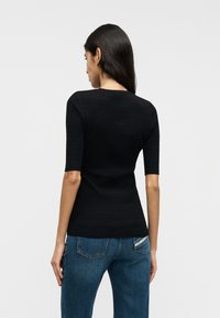 Haut court noir côtelé à manches courtes avec un col rond, une coupe ajustée et un tissu texturé. Associé à un jean en denim bleu avec des poches.