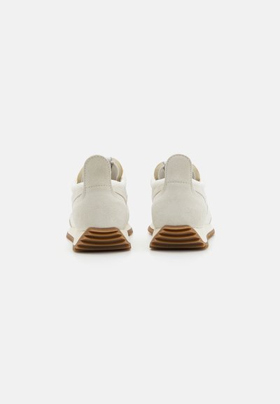 White suede sneakers with a textured heel, rubber outsole, and contrasting brown accents. Minimalist design with a low profile.