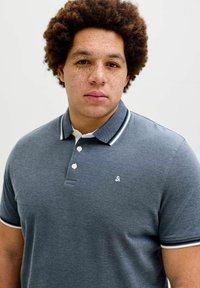 Γκρι πόλο πουκάμισο από υφή υφάσματος, με αντίθετο λευκό γιακά και τρία κουμπιά, μ ε μικρό λογότυπο στο στήθος.