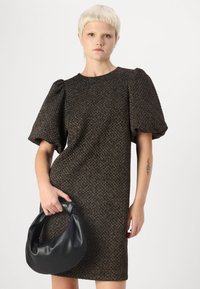 Vestido texturizado castanho com mangas bufantes, decote redondo e silhueta ajustada. A modelo segura uma bolsa preta em forma de crescente.