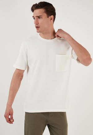 Witte korthands T-shirt met ribbeltextuur, ronde hals en een borstzakje links. Zachte stof en een ontspannen pasvorm.