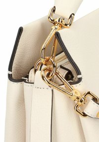 Borsa in pelle color crema con angolo dotato di fibbie metalliche dorate e ganci per tracolla rimovibile, che mostra cuciture dettagliate e superficie testurizzata.