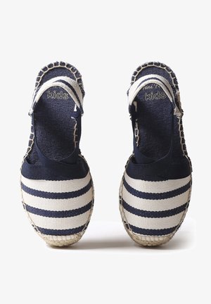 Merine ja valge triibulised laste espadrillid, millel on kangast ülemine osa, elastsed pahkluupanused ja kootud jutepõhjad. Omab õmblusaktsente.