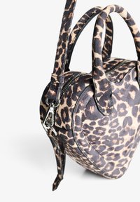 Torba sa printom leoparda u zaobljenom obliku, napravljena od mekog tekstila. Ima dvojne kožne ručke i odvojivu trakicu sa srebrnim detaljima.