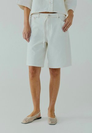 White denim shorts with a relaxed fit, featuring a drawstring, front pockets, and subtle stitching details. Worn with open-weave flats.