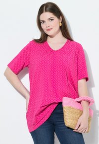 Top rosa de manga corta con un patrón de diamantes y escote en V. Combinado con un bolso de paja tejido que presenta acentos rosas y un asa trenzada.