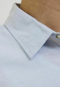 Camisa de color azul claro con un tejido texturizado, que presenta un cierre de botón y un cuello bien cosido.