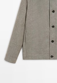 Blazer beige in lino a manica lunga con bottoni, maniche risvoltate e tessuto leggermente strutturato.