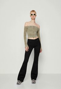 Olivgröna rippade off-shoulder crop top med långa ärmar, kombinerat med svarta utsvängda jeans och grå sneakers. Vita solglasögon och choker.