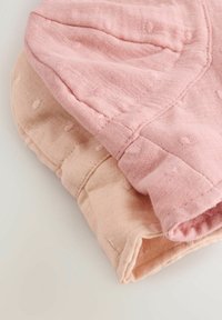 Zwei Stoffstücke in hellrosa und gedämpftem Pfirsich, beide mit einem strukturierten, gepunkteten Muster und rohen Kanten. Weiches, leichtes Material.