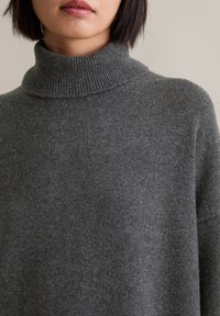 Grijze coltrui gemaakt van zacht breimateriaal, met een geribde kraag en een losse pasvorm, met een gladde, matte textuur.