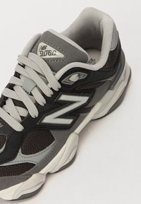 Sneaker grigio e nero con materiali in rete e suede, caratterizzato da un prominente logo "N", lacci in tessuto e suola imbottita.