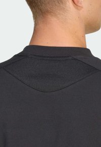 Camiseta de algodón negra con cuello redondeado y un detalle angular texturizado en la parte trasera. Tejido liso con detalles de costura mínimos.