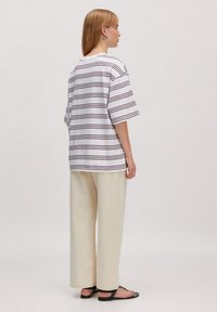 Gestreiftes T-Shirt in Weiß und Dunkelbraun, mit lockerem Schnitt und kurzen Ärmeln, kombiniert mit creamfarbenen, weit geschnittenen Hosen und schwarzen Sandalen.