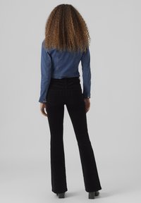 Skraćena traper jakna svijetloplave boje, uparen sa crnim hlačama koje se šire od struka, s pet džepova i glatkom teksturom.