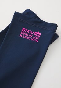 Foldet navy blå stof med pink "BMW Berlin Marathon" tekst og Brandenburg Gate logo trykt på det mod en hvid baggrund.