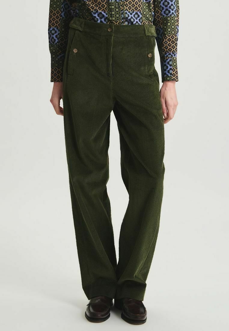 Pantalons en velours côtelé verts à jambes larges, avec une taille haute et deux poches avant, fermés par deux boutons visibles.