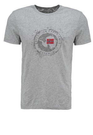 Mand iført en mørk denimjakke over en grå t-shirt med grafik, grå cargoshorts, hvide slip-on sko og solbriller fastgjort til jakkelommen.