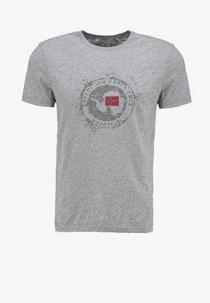 Homme portant une veste en jean foncé sur un t-shirt gris à motif, un short cargo gris, des chaussures blanches sans lacets et des lunettes de soleil accrochées à la poche de la veste.