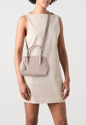 Sac à main en cuir beige clair avec deux poignées et une bandoulière amovible. Présente une surface texturée et un petit détail de tag.