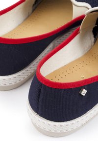 Canvas instappers in marineblauw, met rode rand en witte zool. Beschikt over een glad interieur, geperforeerde binnenzool en een klein metallic logo detail.