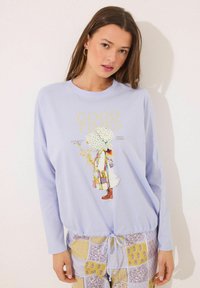Lichtpaarse lange mouwen shirt met een afbeelding van een meisje in een patchwork jurk, met daarboven de tekst "GOEDE TIJDEN." Gecombineerd met een patroonbroek.