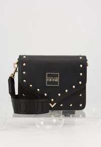 Borsa a tracolla nera in pelle con borchie dorate, dotata di chiusura a patta magnetica e una placca con logo. Include una tracolla regolabile con motivo.
