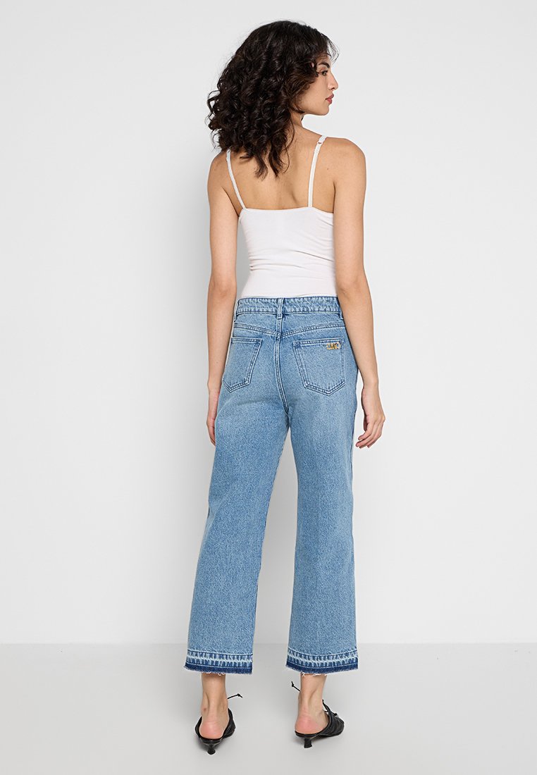 Jeans de pierna ancha de tiro alto en azul claro con dobladillo deshilachado y detalles de costura sutiles. Combinado con una camiseta sin mangas blanca sencilla.