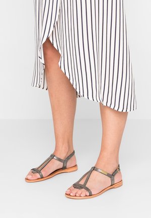 Sandales à lanières en gris métallique avec une semelle en bois. Caractérisées par un design en T et une brillance subtile. Associées à une robe rayée.