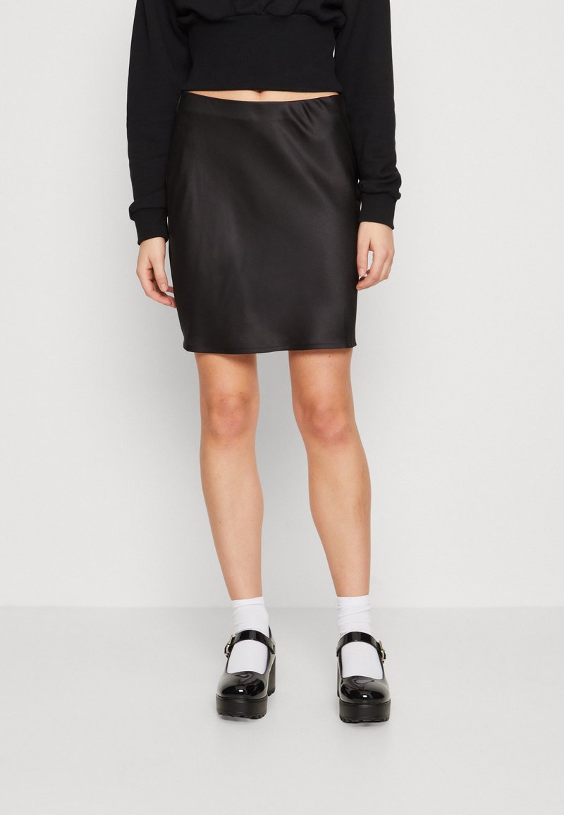 Mini falda negra de satén con una textura suave y forma ligeramente ajustada, combinada con zapatos de plataforma negros y calcetines blancos.