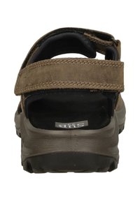 Brown suede sandal with adjustable strap, rubber sole, cushioned footbed, and prominent stitching details. Rear view showcases design and comfort.