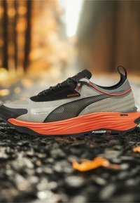 Scarpa da ginnastica leggera grigia con accenti neri e arancioni, caratterizzata da una tomaia testurizzata e una suola arancione ben ammortizzata.