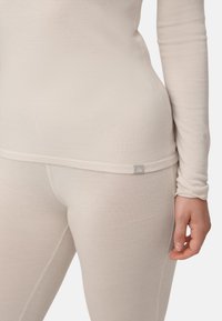 Lysebeige langærmet top og tætsiddende leggings lavet af blødt, elastisk stof. Indeholder diskret logoetiket ved kanten af toppen og leggingsene.