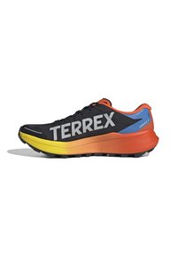 Schwarzer Sportschuh mit großem grauem "TERREX"-Schriftzug, Mittelsohle mit gelb-orangefarbenem Farbverlauf, blauem Fersenbereich und orangefarbener Umrandung, entworfen für Trailrunning.