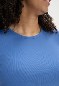 Blue ribbed knit top with a crew neckline, featuring a soft texture and fitted design, captured from the shoulder to neck area.
