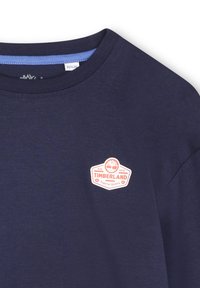 Navyblauwe katoenen t-shirt met een ronde hals, voorzien van een rood-wit Timberland-logo op de borst. Gladde textuur, korte mouwen.
