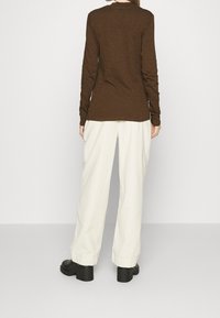 Lange mouwen bruine top met een ontspannen pasvorm, gecombineerd met witte wijde broek en zwarte chunky hakken. Minimalistisch ontwerp, effen kleuren.