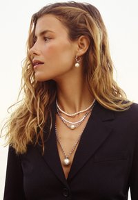 Sølv kædelykke med flere lag, der har små og store perler. Elegante dråbeøreringe med perle detaljer. Mørk blazer.