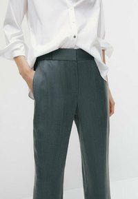 Pantalon léger gris avec une texture lisse et des poches latérales, associé à une chemise blanche à boutons, avec des manches retroussées.