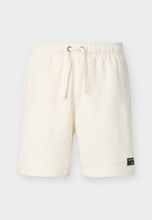 Kremfargede, avslappede shorts med elastisk midjebånd, snor, sidelommer og en liten svart merkeetikett nederst på venstre benkant.