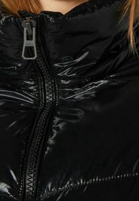Černá péřová bunda s lesklým povrchem, vybavená středn�ím zipem a zvýrazněnými švy, zdůrazňující elegantní a moderní design.