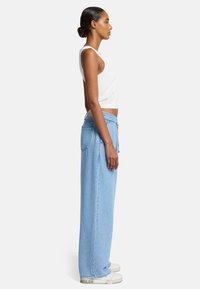 Lichtblauwe denim broek met wijde pijpen en een ontspannen pasvorm, gecombineerd met een witte, aansluitende tanktop. Beschikt over een trekkoord in de taille en minimale details.