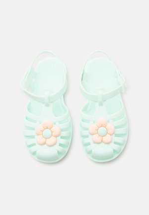 Jasnoniebieskie sandały dziecięce z paskami wokół kostki i brzoskwiniowymi ozdobami w kształcie kwiatów na palcach, widziane z góry.