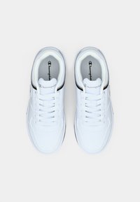 Λευκά αθλητικά παπούτσια με λείο συνθετικό επάνω μέρος, κορδόνια και μαύρες λεπτομέρειες στις πλευρές. Μαλακοί πάτοι και υφασμένες λαστιχένιες σόλες.