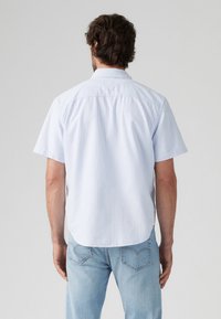 Korteblauwe, met witte verticale strepen bedrukte, coll Polo-shirt met korte mouwen. Heeft een afgeronde onderkant en een ontspannen pasvorm. Lichtgewicht stof.