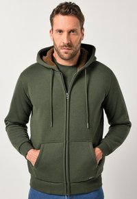 Olivgrüner Zip-Hoodie aus weichem Material, mit einer braunen Fleece-fütterten Kapuze, Kordelzügen und Fronttaschen.
