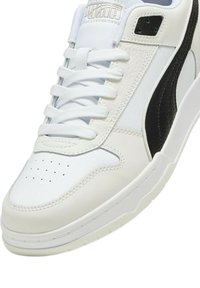Sneaker in pelle bianca con accento nero. Presenta materiali testurizzati, punta rotonda, perforazioni e lacci piatti. Collo regolabile per una vestibilità ottimale.