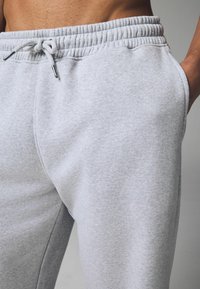 Graue Sweatpants aus weichem Stoff mit elastischem Bund, Kordelzugverschluss und Seitentaschen; glatte Textur mit lässiger Passform.