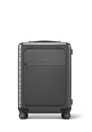 Valise rigide de couleur gris foncé avec un design élégant, dotée d'une poche zippée à l'avant, d'une surface texturée et de roulettes doubles pivotantes.