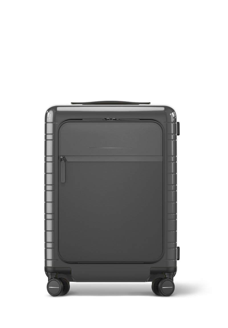 Valise rigide de couleur gris foncé avec un design élégant, dotée d'une poche zippée à l'avant, d'une surface texturée et de roulettes doubles pivotantes.